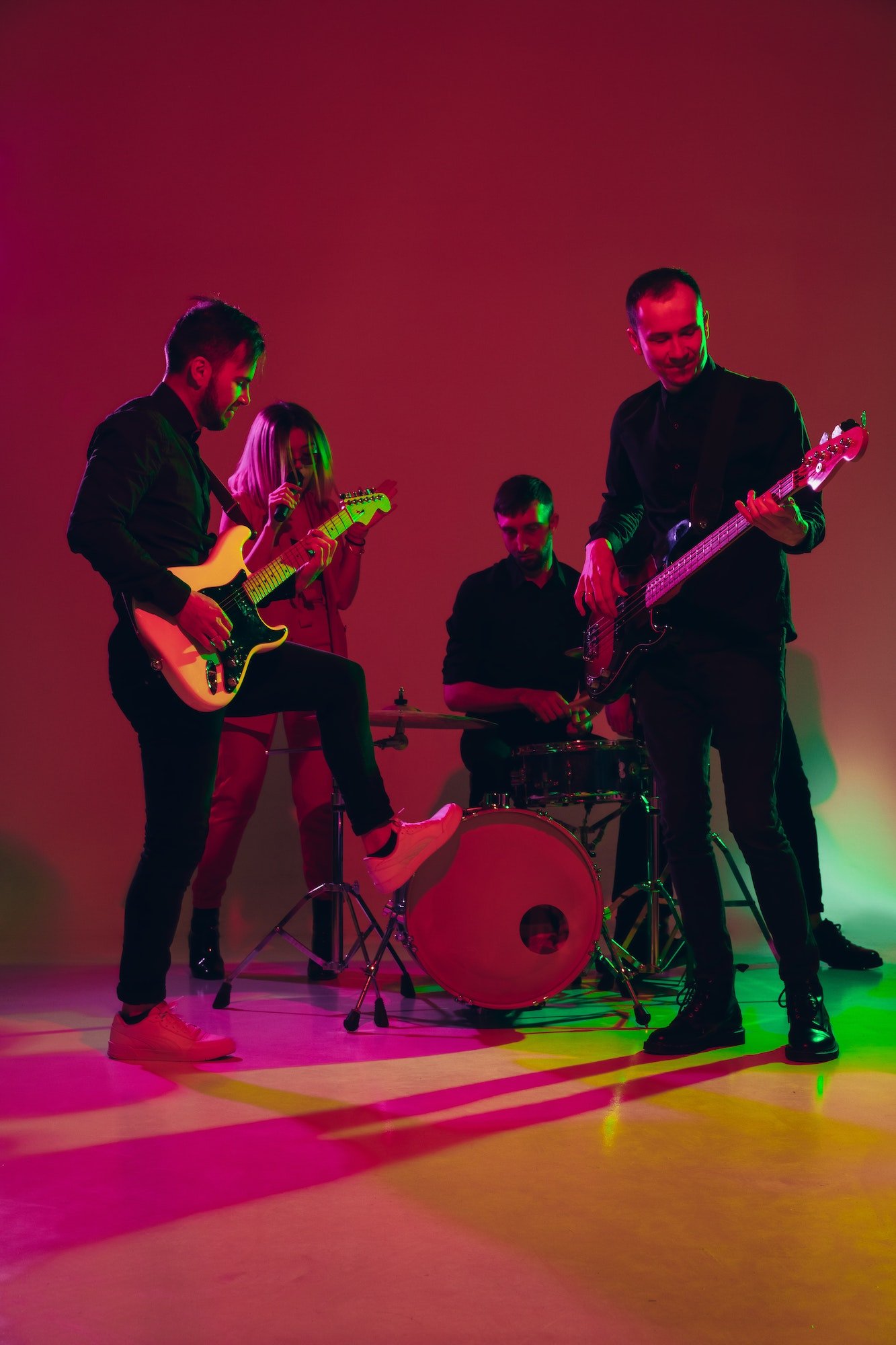 Young caucasian musicians, band performing in neon light on red studio background